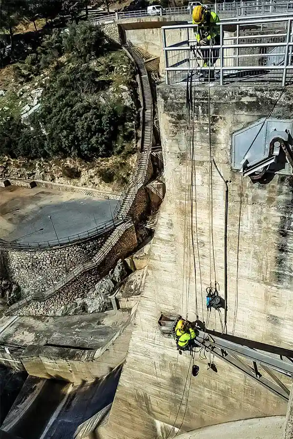 Operarios suspendidos realizando labores de supervisión y mantenimiento en una presa de obra civil.